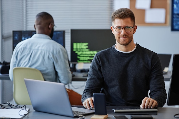 Portrait of male software developer smiling at camera tout en étant assis sur le lieu de travail dans l'espace de copie de bureau