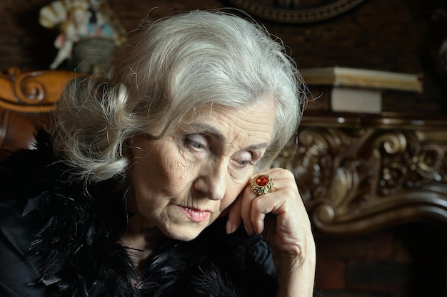 Portrait of sad senior woman in boa posant à la maison