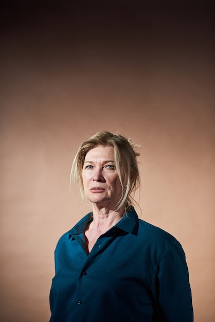 Portrait of senior businesswoman in blue blouse posing at camera isolé sur fond marron