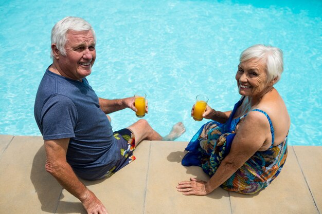 Portrait of senior couple holding verres à jus près de la piscine