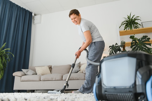 Portrait of senior woman avec aspirateur à l'intérieur à la maison hoovering