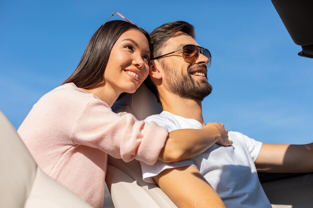 Portrait of smiling asian girl emvracing caucasian guy driving cabriolet