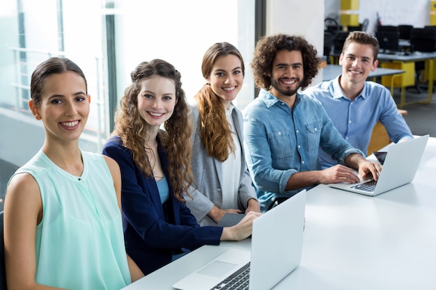 Portrait of smiling business team discuter sur ordinateur portable en réunion