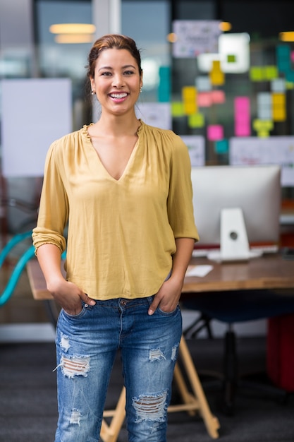 Portrait of smiling female executive standing with hands in pocket