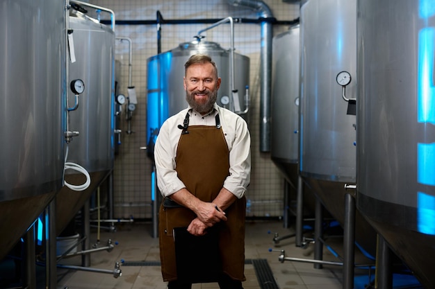 Portrait of smiling man brasseur en tablier debout parmi les cuves de distillerie