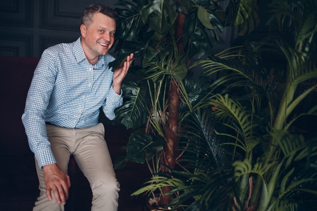 Portrait of smiling senior middle adult man in blue shirt holding leaf green plant looking at camera. Plantes de jardinage.