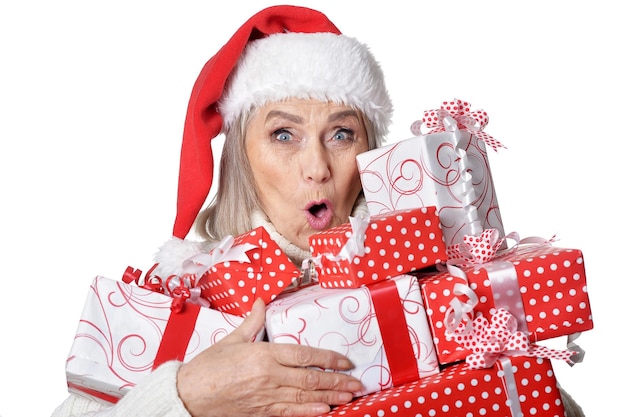 Photo portrait of smiling senior woman in santa hat posant avec des cadeaux sur fond blanc