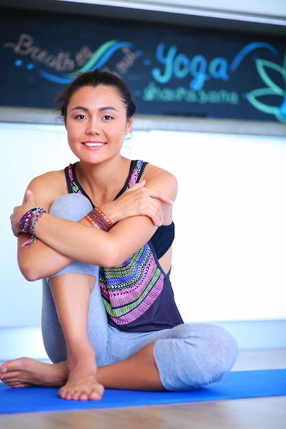 Portrait of smiling yoga woman sitting at yoga mat après l'entraînement au studio de yoga