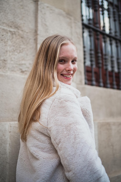 Portrait of smiling young blonde woman looking at camera Elle porte un manteau blanc tout en marchant