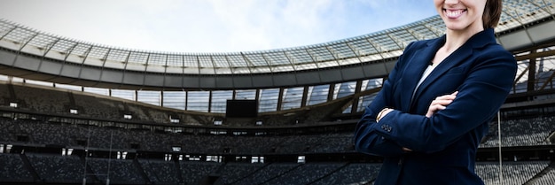 Photo portrait of smiling young businesswoman bras croisés contre le stade de rugby par beau temps