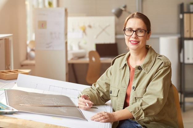 Portrait of smiling young woman dessin de plans et de plans tout en travaillant au bureau au bureau d'ingénieurs,