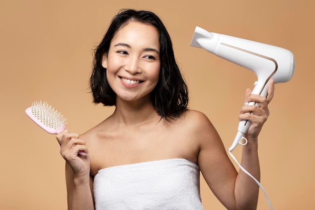 Portrait of smiling young woman sèche ses cheveux et à l'aide d'une brosse sur fond beige