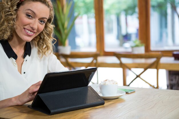 Portrait of smiling young woman using digital table at table in coffee shop