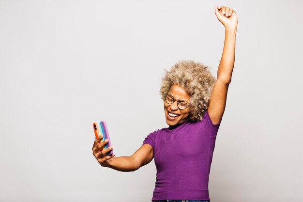 Portrait of Smiling Young woman using smart phone avec un cas de drapeau arc-en-ciel en se tenant debout contre Wh