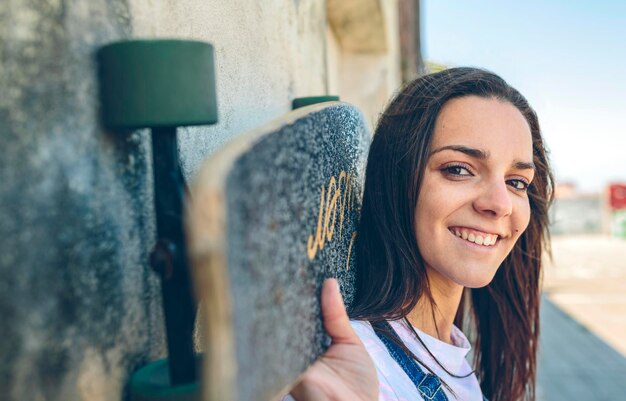 Portrait of smiling young woman with skateboard sur ses épaules