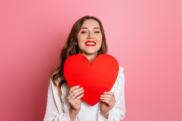 Portrait of a woman holding big red heart card isolé sur fond rose