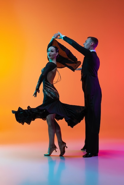 Portrait of young couple dancing tango isolé sur fond orange dans les néons