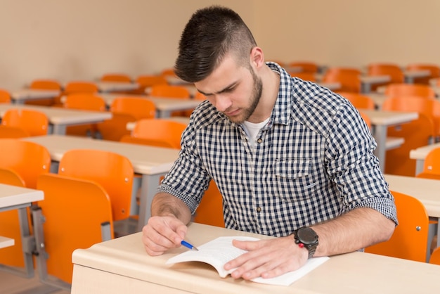 Portrait Of Young Male College Student With Book Sitting in Classroom Only