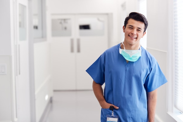 Portrait Of Young Male Doctor Wearing Scrubs debout dans le couloir de l'hôpital