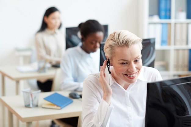 Portrait d'opérateurs de hotline féminine assis à un bureau en ligne, se concentrer sur une femme souriante parlant au client via un casque