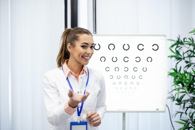 Portrait d'une opticienne professionnelle pointant sur le tableau des yeux diagnostic de la vision en temps opportun