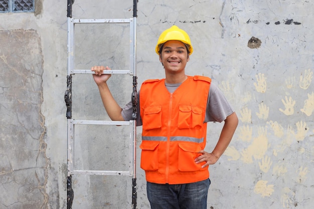 Portrait d'un ouvrier de la construction souriant à la caméra tout en tenant une échelle sur un chantier en plein air