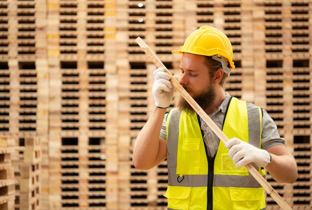 Portrait d'un ouvrier dans une usine de menuiserie sent le bois sur fond de palettes en bois