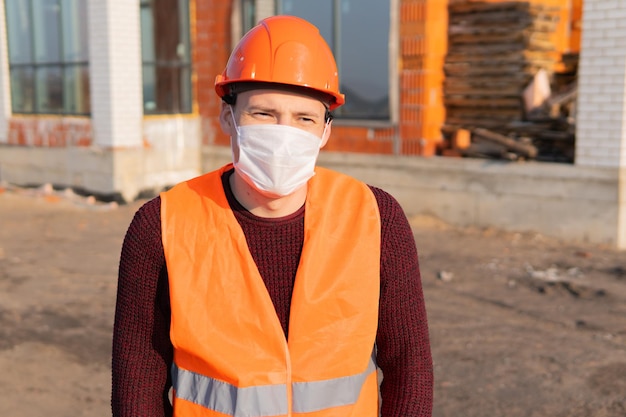 Portrait d'un ouvrier du bâtiment portant un masque médical et une combinaison sur fond de maison en construction