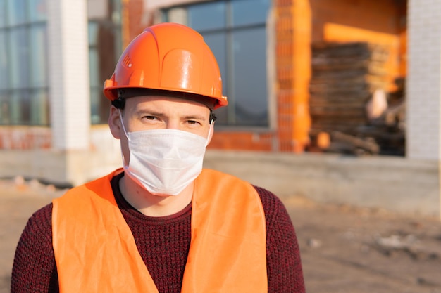 Portrait d'un ouvrier du bâtiment portant un masque médical et une combinaison sur fond de maison en construction