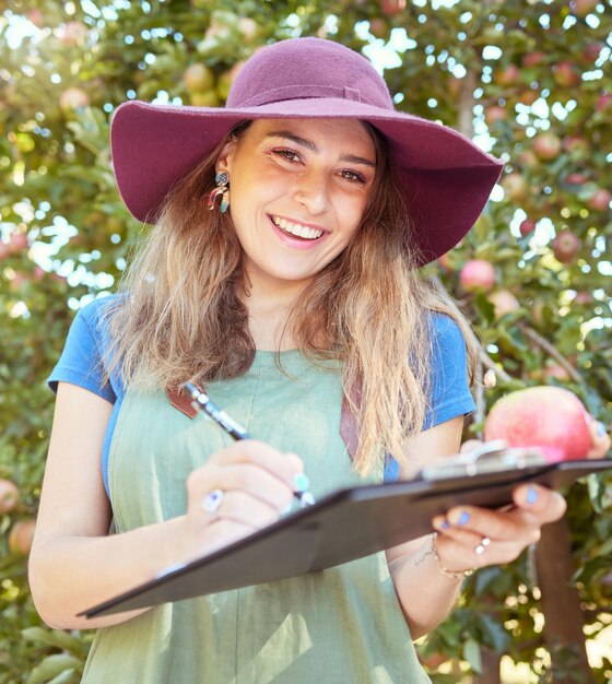 Portrait d'une ouvrière agricole tenant une pomme tout en écrivant et en prenant des notes sur une ferme de verger pendant la saison des récoltes Agronome faisant l'inspection et la tenue de registres sur la qualité des produits