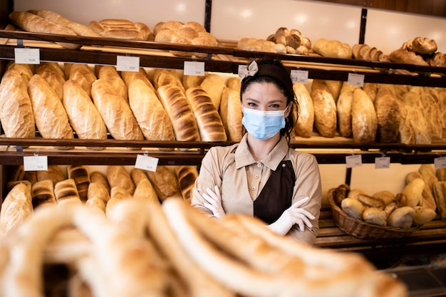 Portrait d'une ouvrière de boulangerie portant un masque facial et vendant des pâtisseries dans une boulangerie