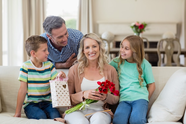 Portrait de parents et d'enfants assis sur un canapé avec présent dans le salon