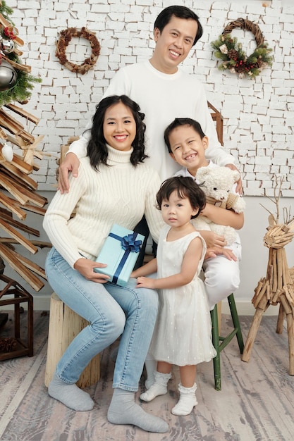 Portrait de parents souriants et de leurs deux enfants posant pour une photo de famille dans une maison décorée pour Noël