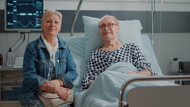 Portrait d'un patient âgé et d'une femme assis dans une salle d'hôpital. Homme âgé malade allongé dans son lit et vieille femme aidant à se rétablir dans la salle de soins intensifs de la clinique.