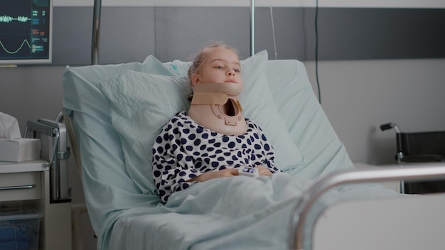 Portrait d'un patient enfant malade allongé dans son lit regardant la caméra tout en ayant un collier cervical en convalescence après une chirurgie médicale douloureuse dans une salle d'hôpital. Enfant portant un tube nasal pendant l'examen