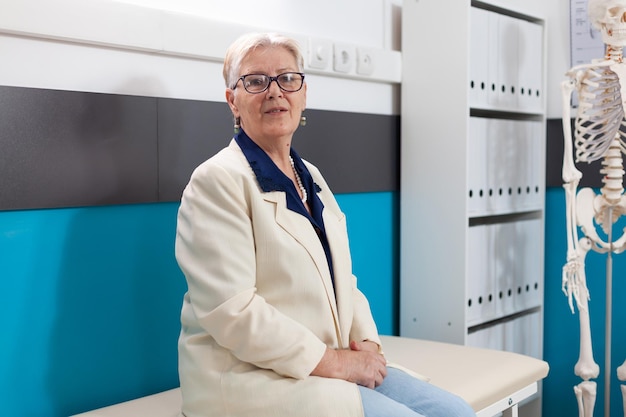 Portrait d'une patiente âgée à la retraite malade debout sur son lit dans un bureau de l'hôpital regardant la caméra en attendant l'expertise de la maladie lors d'un rendez-vous médical. Soutien aux services de médecine