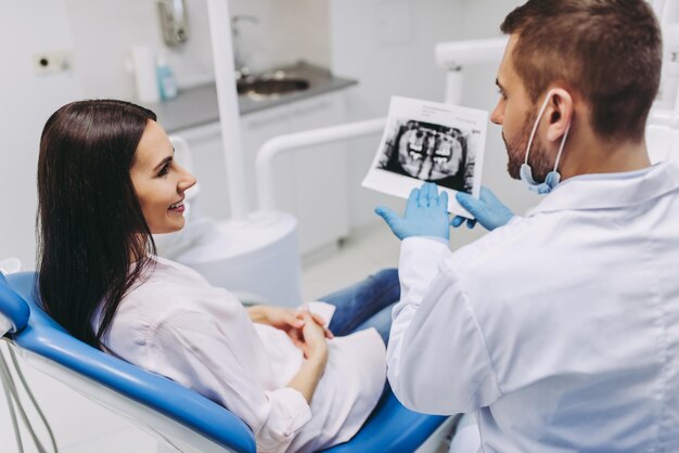 Portrait d'une patiente parlant avec un dentiste masculin regardant une radiographie dans une clinique moderne