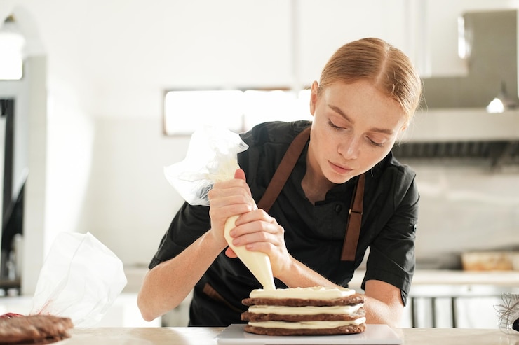 Photo portrait d'une pâtissière appliquant de la crème au beurre sur une couche de gâteau au chocolat