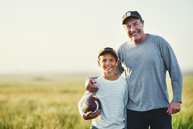 Portrait de père enfant et ballon de rugby dans un champ de campagne pour créer des liens et s'amuser dans la nature Maquette papa et jeune enfant avec bonheur et sourire prêts pour un jeu actif sportif en plein air à la ferme