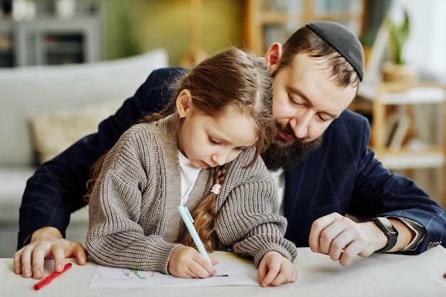 Portrait d'un père juif attentionné dessinant des images avec sa fille à la maison