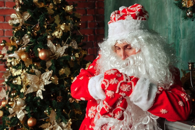 Portrait d'un père Noël émotionnel avec sac de cadeaux par cheminée de Noël dans un salon décoré avec arbre de Noël. Le Père Noël vient et apporte des cadeaux la nuit. Espace de copie pour le site