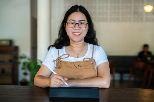 Portrait de personnes indépendantes asiatiques femme d'affaires portant des lunettes élégantes hipste Dessiner ou prendre note sur une tablette numérique avec un stylo électronique pour naviguer sur Internet, discuter et bloguer dans un café