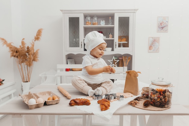 Portrait de petit enfant adorable caucasien portant une toque. Un bébé mignon est assis dans la cuisine à la maison.