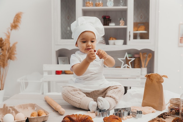 Portrait de petit enfant adorable caucasien portant une toque. Un bébé mignon est assis dans la cuisine à la maison.