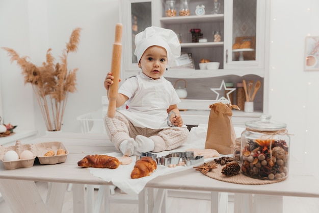 Portrait de petit enfant adorable caucasien portant une toque. Un bébé mignon est assis dans la cuisine à la maison.