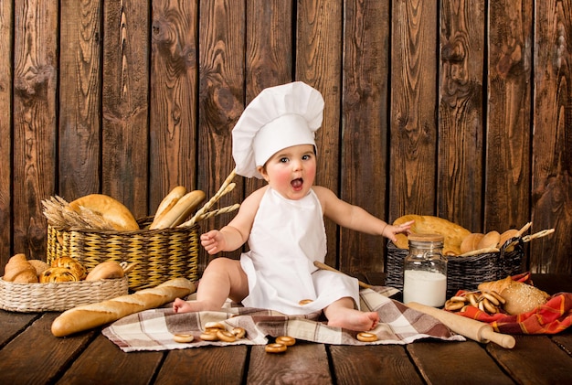 Portrait d'un petit enfant dans les vêtements du chef parmi les produits de boulangerie sur un fond en bois