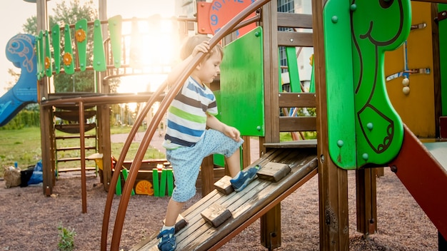 Portrait d'un petit garçon actif rampant et grimpant sur un escalier en bois sur une aire de jeux pour enfants au parc