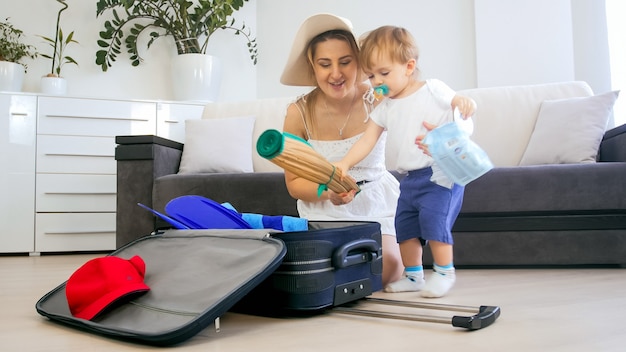 Portrait d'un petit garçon aidant la mère à emballer des choses dans une valise pour un voyage de vacances.