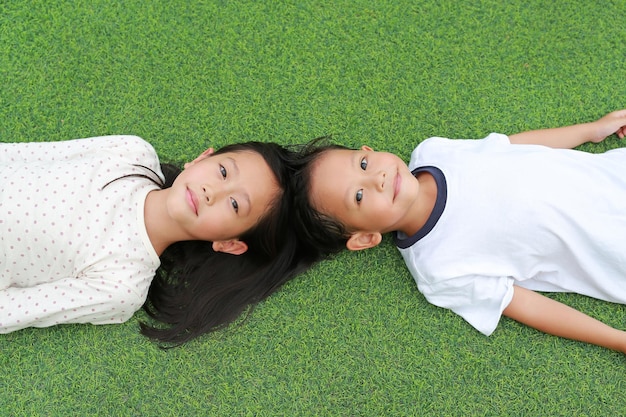 Photo portrait d'un petit garçon asiatique et d'une fillette allongée sur fond d'herbe verte ensemble