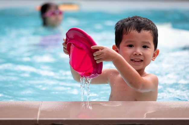 Portrait de petit garçon asiatique regardant la caméra et souriant tout en jouant de l'eau dans la piscine. Activité estivale et concept de mode de vie de l'enfance.